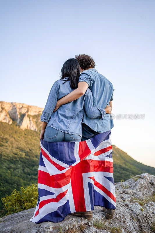 幸福的夫妇举着英国国旗站在山顶，后视镜