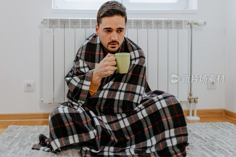 男人冻在家里，盖着毯子坐在那里喝热茶