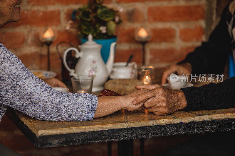 深情的老夫妇手牵着手，在他们的露台上浪漫地享受下午茶