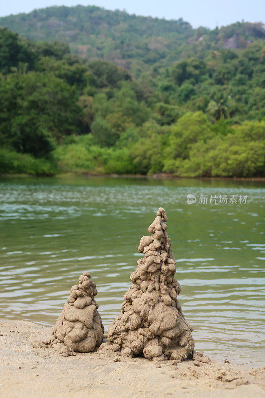 图像滴沙城堡塔在沙滩低潮水的边缘，重点在前景