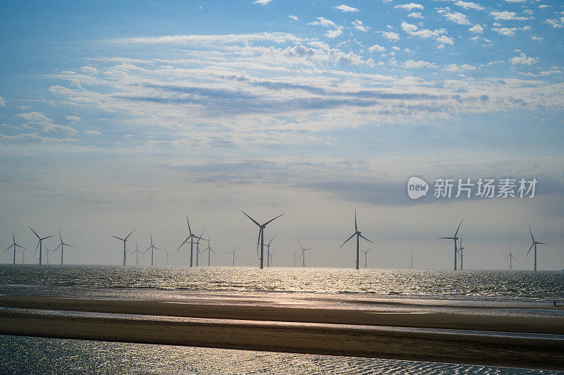 风力涡轮机的风扇在波光粼粼的海面上旋转。蓝天白云。