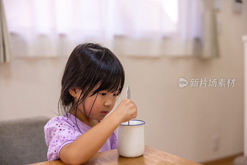 小女孩正在用勺子搅拌一杯牛奶