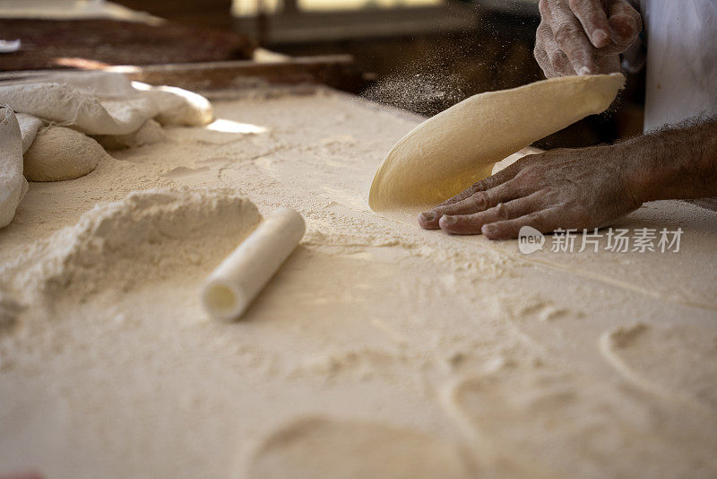 一个老人在面包店做面包，把面团铺好