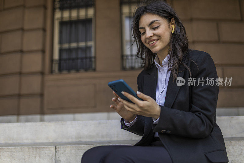 美丽的女孩心满意足地笑着，坐在一栋旧建筑的楼梯上，给她的同事写信，说她成功地完成了一天的工作。