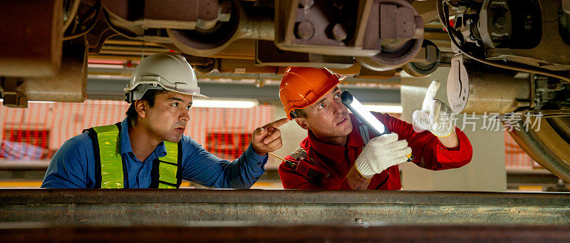 工程师和技术工人在火车工厂工作场所用灯管进行检查和维修的全景图。