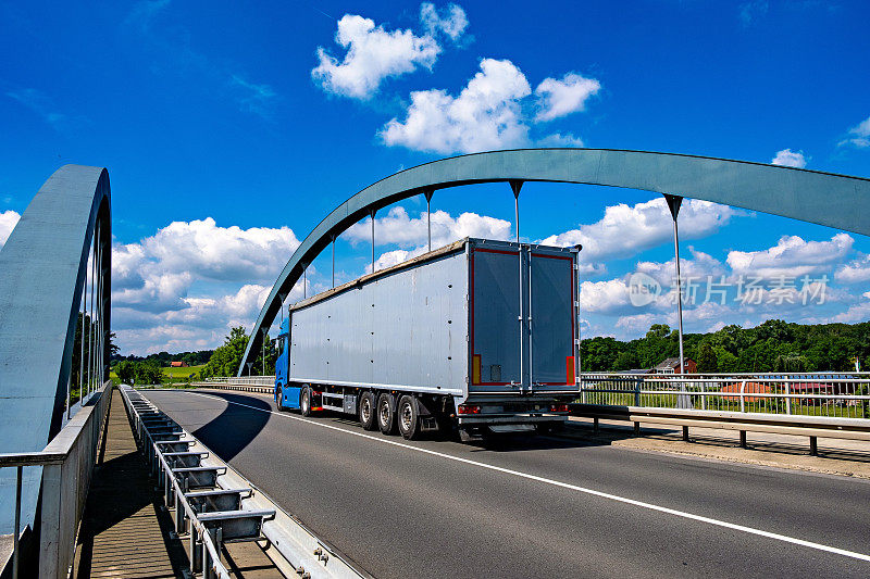 大钻机美国半挂车运输商业货物在冰箱半挂车行驶在桥上的高速公路上，蓝天为背景