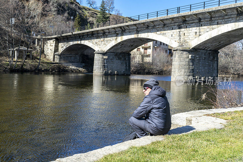 一个孤独的人坐在河岸上凝视着风景。