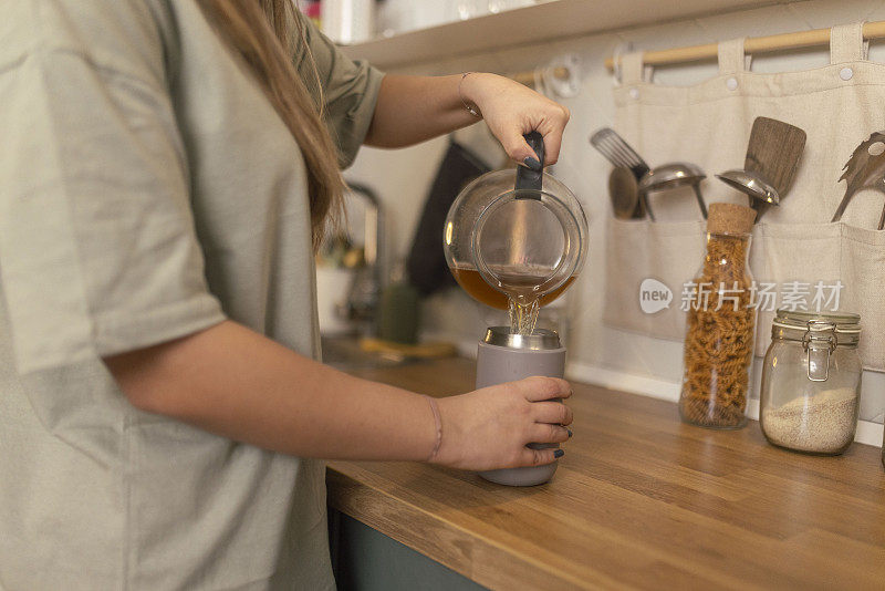 泡好凉茶后，这位女士把茶从水壶里倒进可重复使用的杯子里