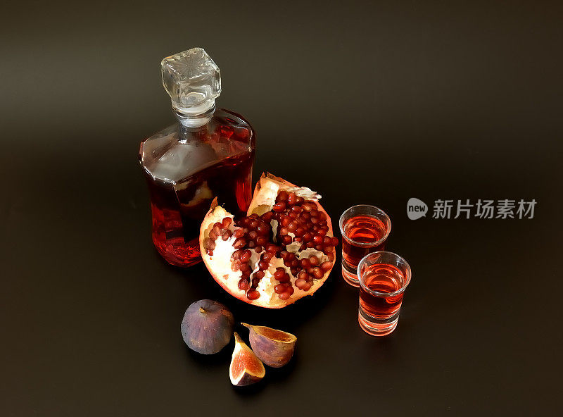 黑色背景的无花果石榴利口酒，一瓶烈酒，两杯，周围是成熟的水果。