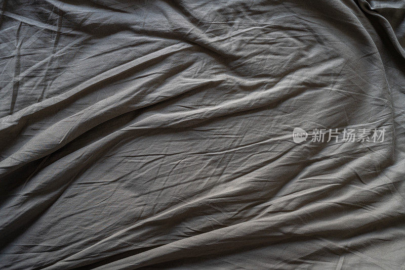 皱巴巴的灰褐色床单。全画幅纺织品背景。面料质地。