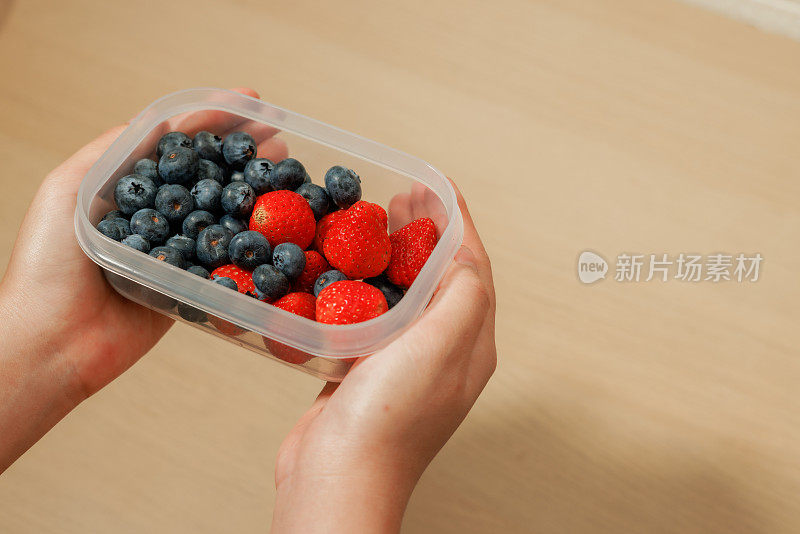 背景是手拿蓝莓和草莓装在回收塑料盒里。