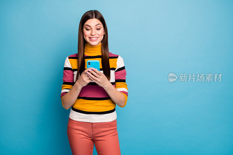 正面开朗的女孩使用智能手机阅读社交网络信息分享评论反馈穿时尚的红色套头衫孤立在蓝色背景
