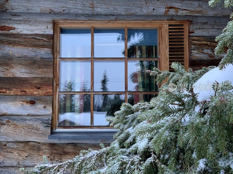 一扇窗在一座木屋里，旁边是一棵美丽的冷杉树在雪地里。