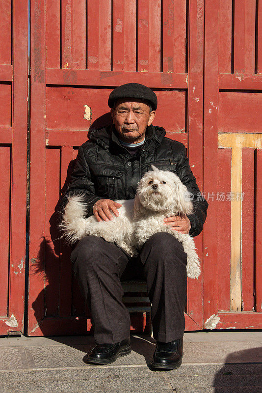 一个老人和他的狗在外面的胡同里休息。