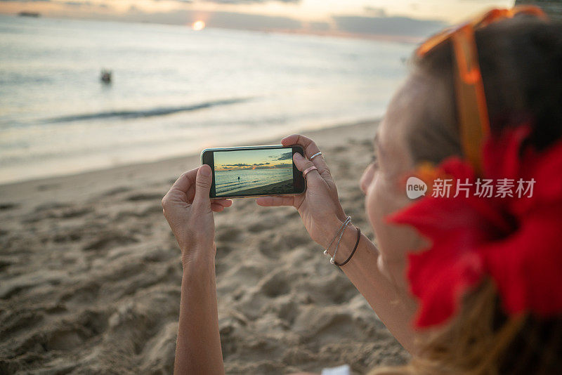 年轻女子用手机在海滩上拍摄日落