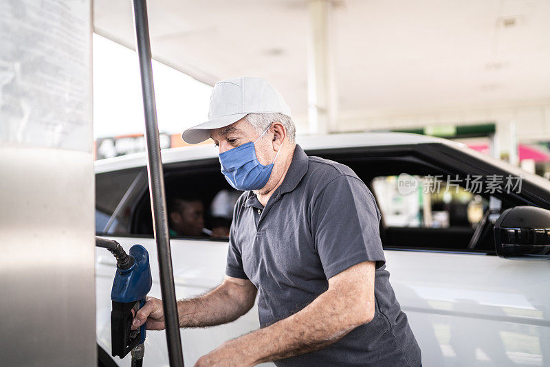 一位戴着面罩的老人在加油站给一辆车加油