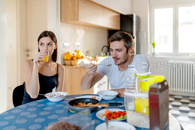 一个年轻人在吃早餐麦片，他女朋友在喝果汁