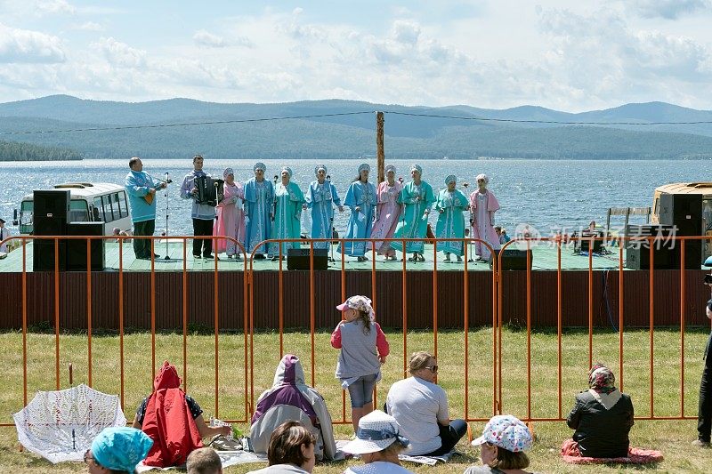 卡拉塔格音乐节上，观众们在观看以湖为背景的舞台上的女子入场。