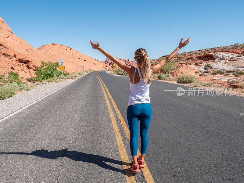 快乐的女孩站在路中间，内华达州空荡荡的高速公路上的女人