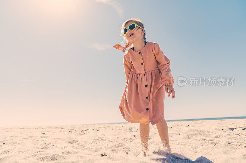 一个五岁的小女孩微笑着在晴朗无云的日子里在沙滩上跑步。