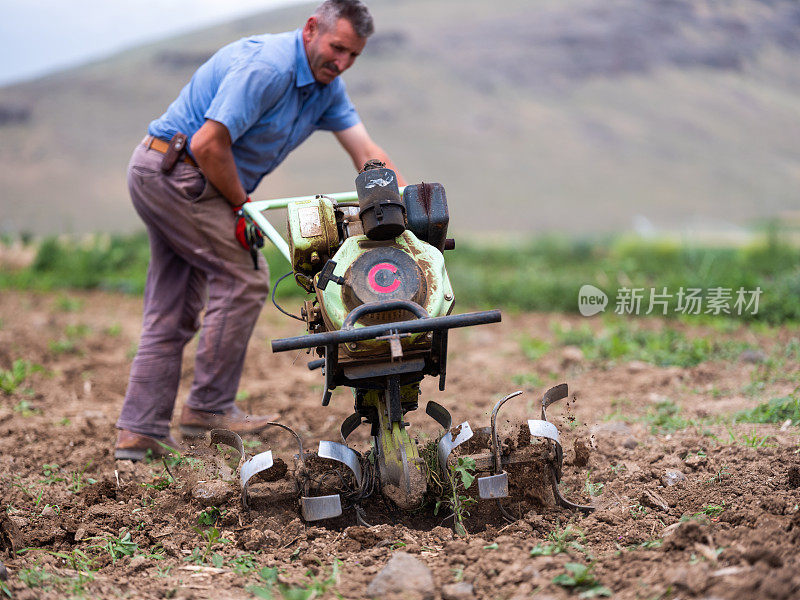 一位男性农民用一辆汽油步式拖拉机犁地