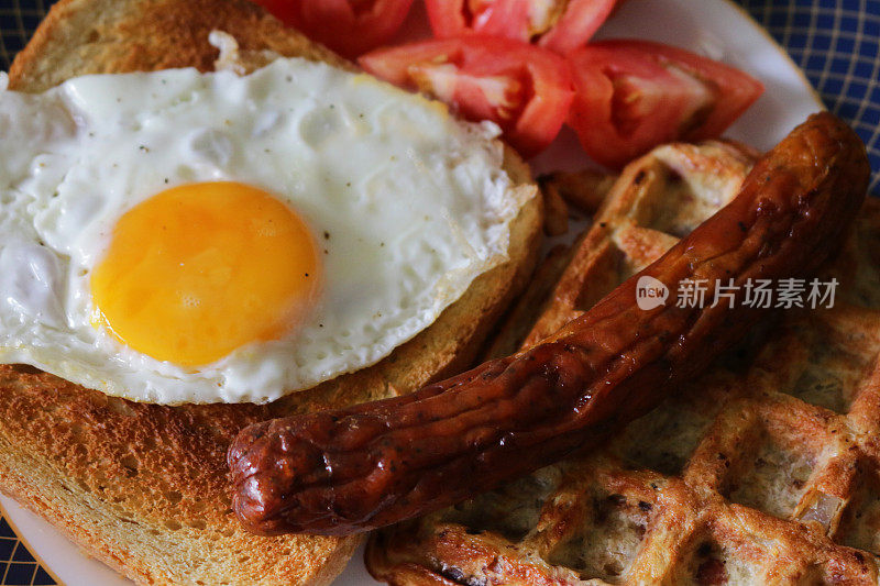 特写图像显示元素的完整的英国早餐油炸香肠，华夫饼，煎蛋，生番茄和白色吐司在一个盘子，俯瞰