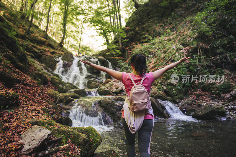 一个女人站在瀑布边，双手高举