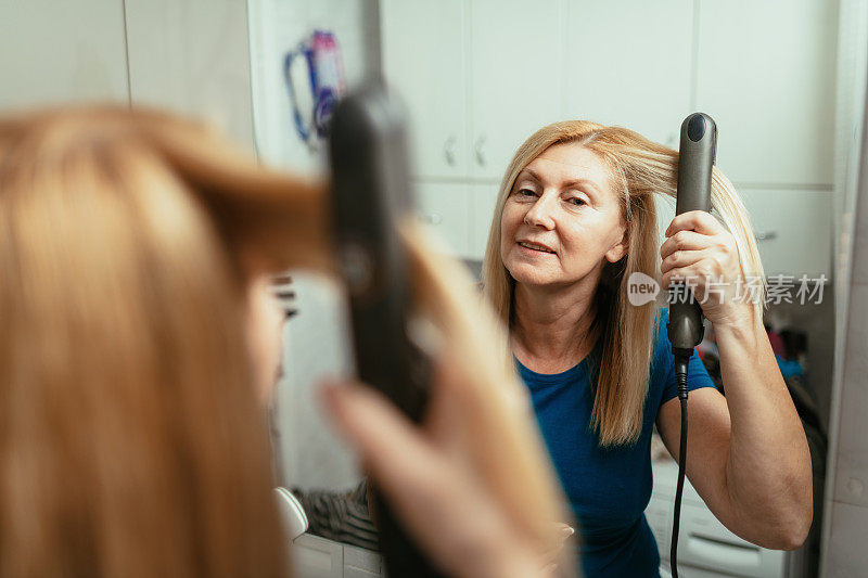 成熟的女性在家美容-在镜子前烫头发