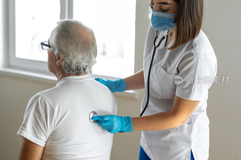 年轻女医生用听诊器检查年长男病人的背部