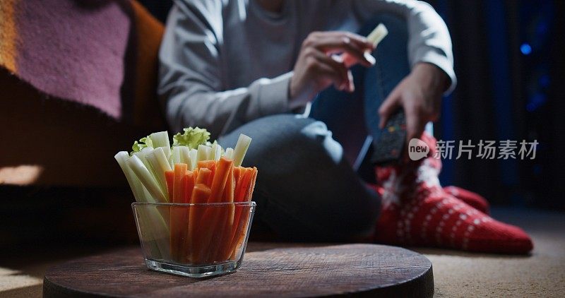 女人坐在地上，一边看电视一边吃芹菜和胡萝卜条