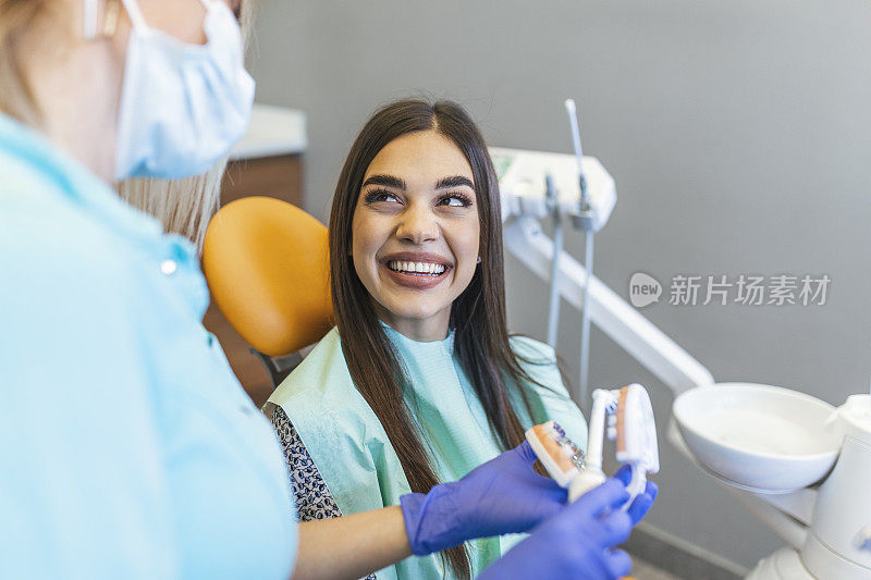 漂亮的牙医女医生在牙科诊所刷下巴模型，牙科保健概念。牙科保健的概念。年轻女牙医在牙科诊所展示女病人下颌模型