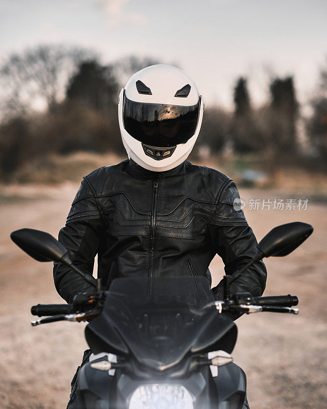 一个年轻人的肖像，坐在摩托车上，穿着皮夹克和头盔。