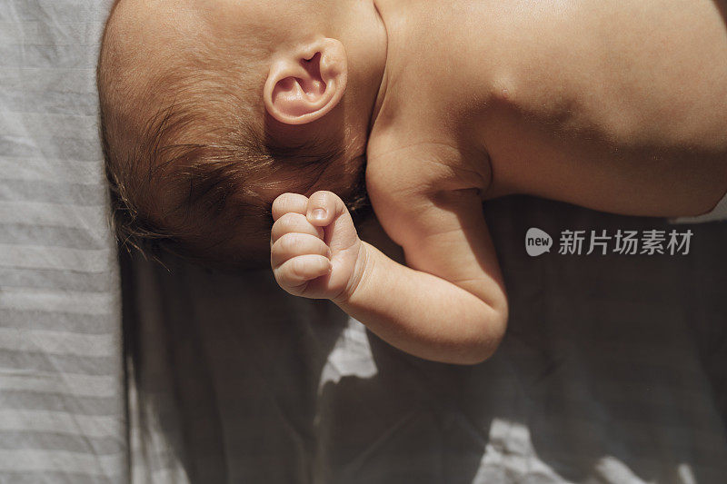 与新生儿亲密:一个不认识的婴儿在床上握着一个拳头