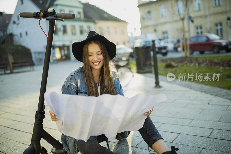 漂亮的女人骑着电动踏板车在地图上寻找方向