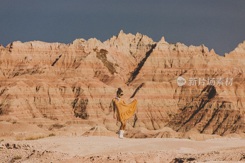 在干旱的沙漠气候中，一名女子在山峰前穿着衣服摆姿势