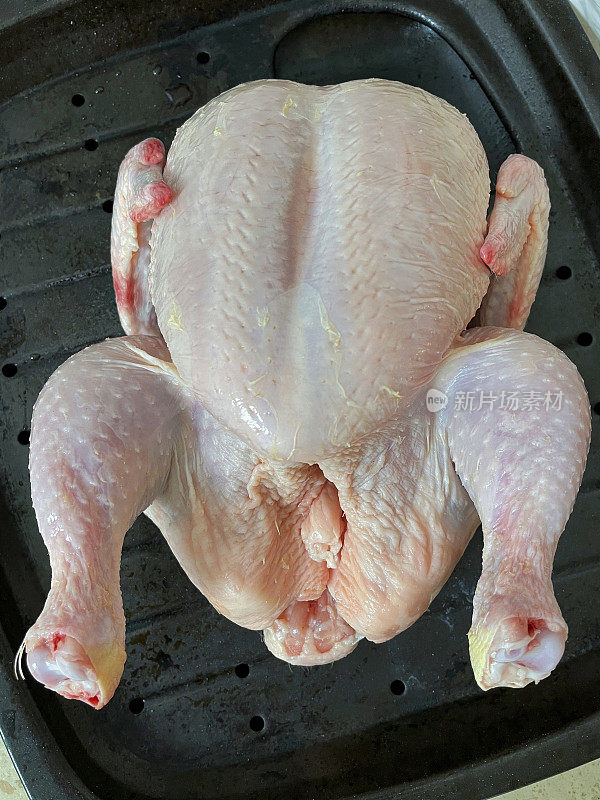 整只鸡放在厨房工作台上的烤箱托盘里，准备放在烤箱里烤，高架视野