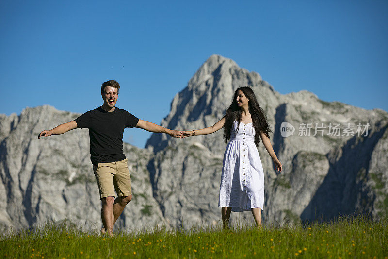 幸福的年轻夫妇手牵着手，在山间草地上奔跑