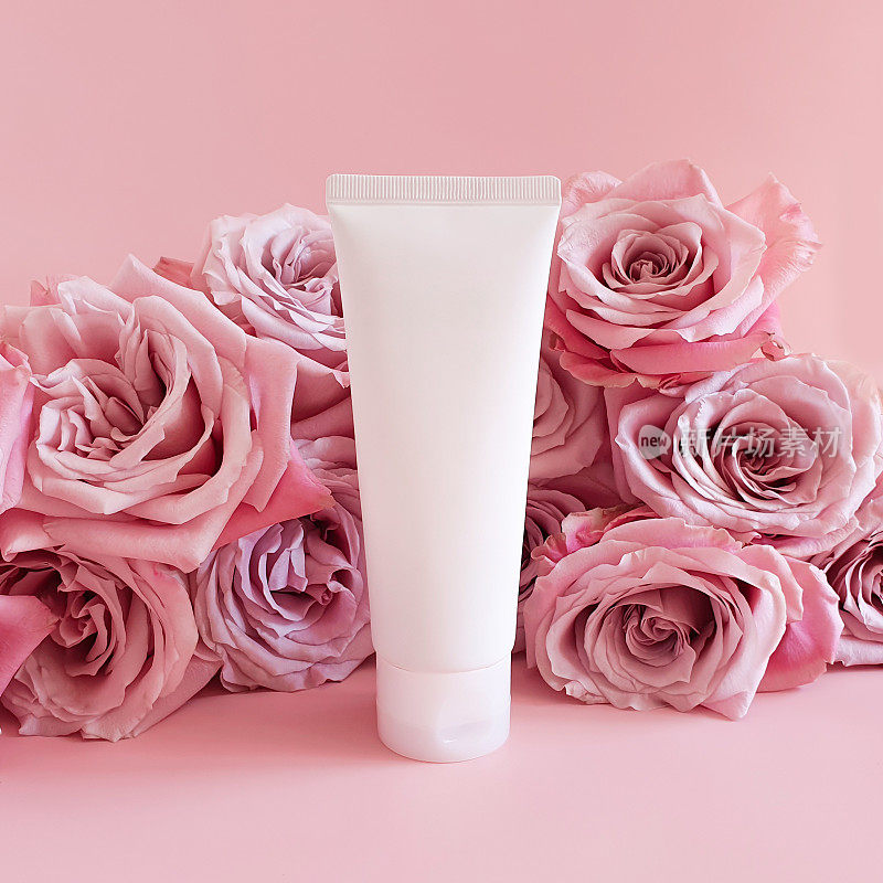 白色挤压瓶塑料管的模型，用于医药或化妆品品牌-奶油，凝胶，护肤品，牙膏和粉红色的玫瑰花在粉红色的背景上。生物有机美容空白，正面