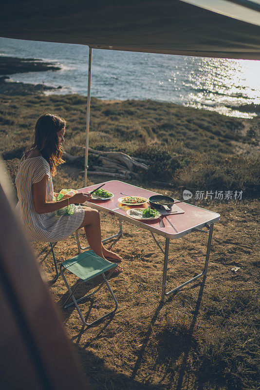 一位年轻女子在海边的野餐桌上吃早餐