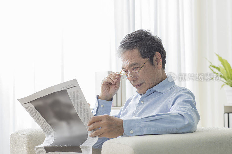 老年男人坐在沙发上看报纸