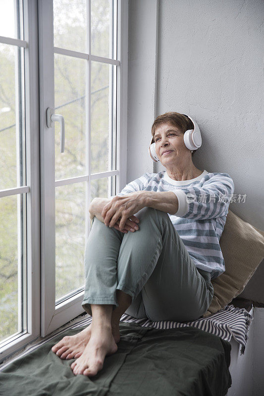 音频愈合。概念没有压力。老妇人戴着耳机在家听音乐。
