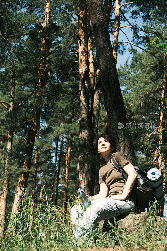 图为一名女背包客在森林中徒步旅行时在石头上休息