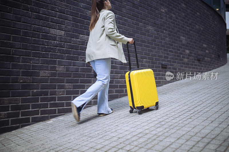 为了准时到达车站，这位妇女拖着她的手提箱快速地走着。