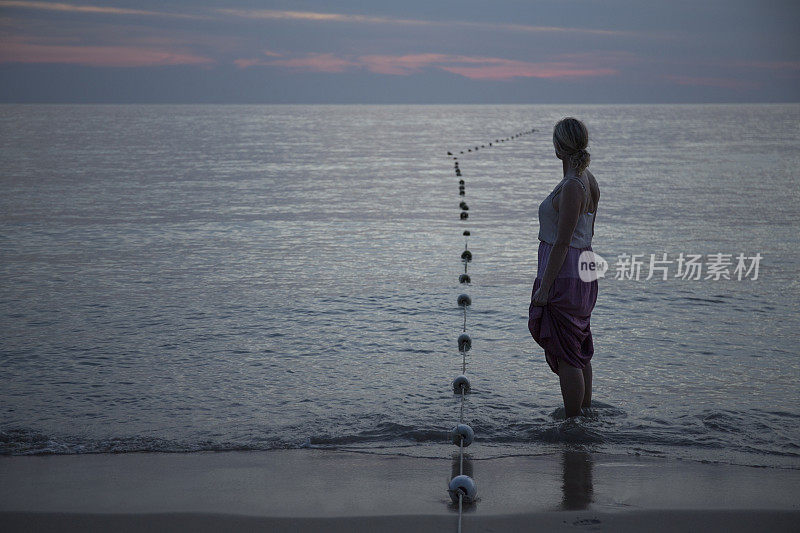 黄昏时分，一名女子在海滩上驻足观赏大海