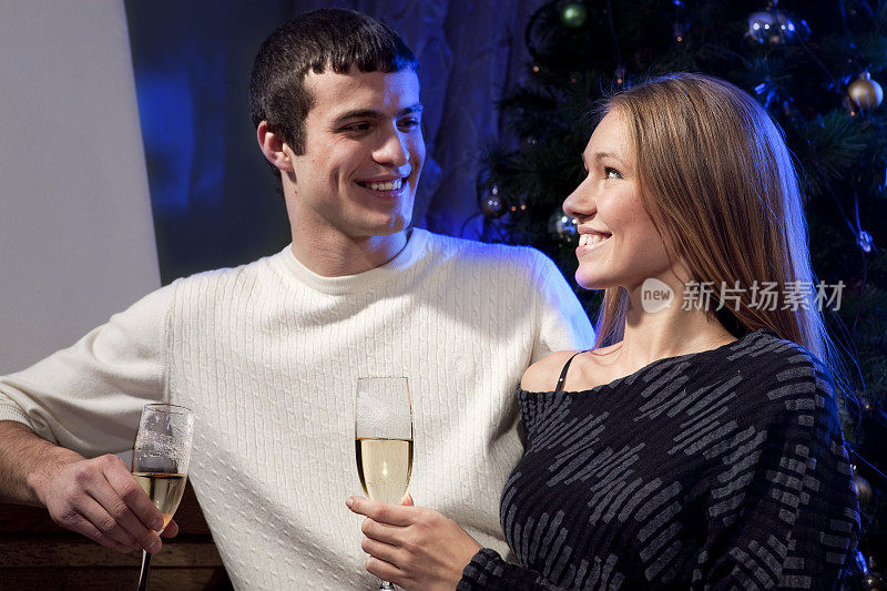微笑的夫妇在圣诞树旁用香槟敬酒。