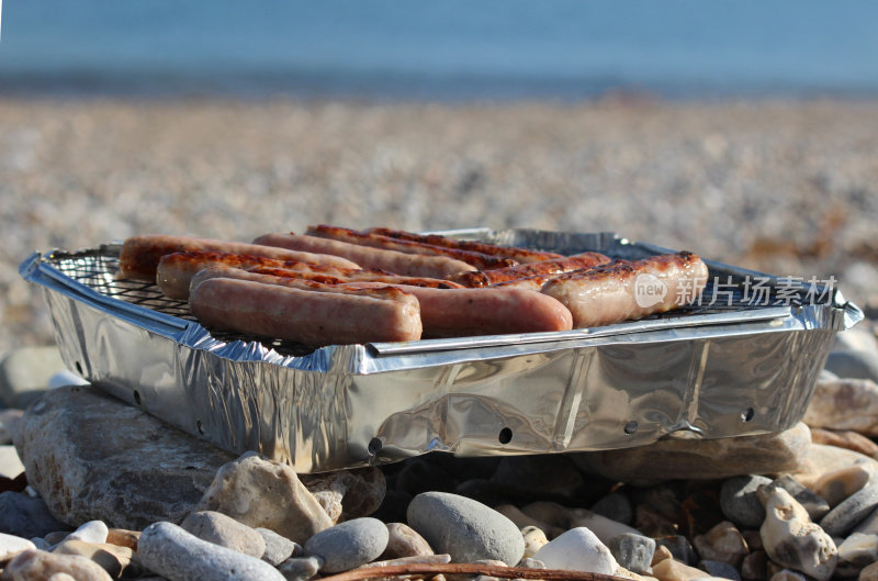 卵石海滩的图像海边用一次性烧烤烹饪香肠