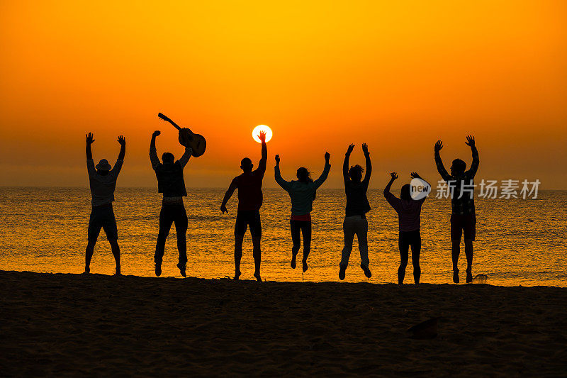 日落时分，欢乐的朋友们在海滩上跳跃的剪影