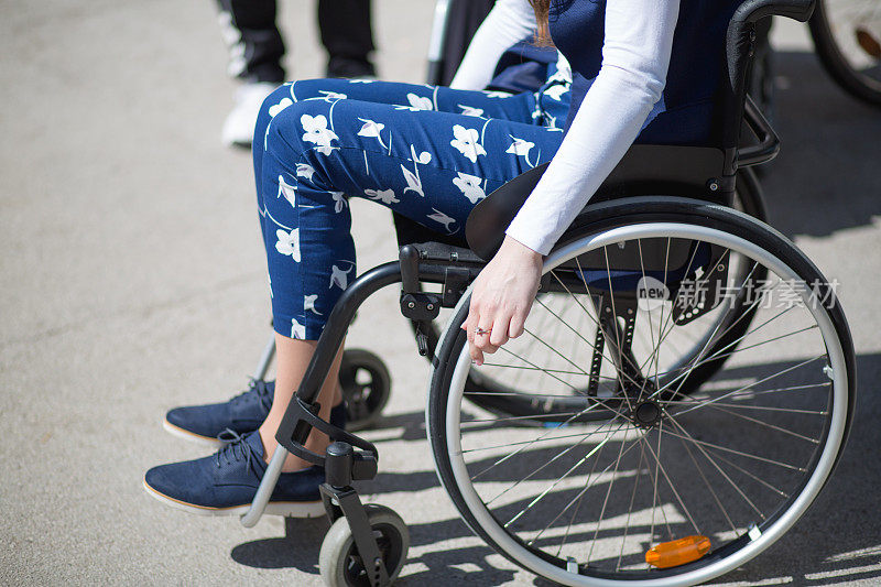 残疾的年轻女子坐在轮椅上在沥青球场上玩地滚球。
