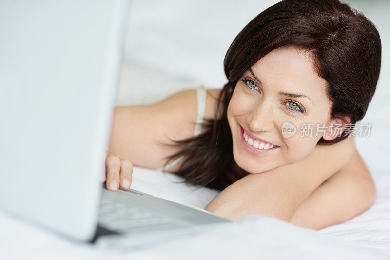 微笑的白人女人躺在床上拿着笔记本电脑