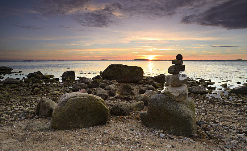 日落时，在狂野的岩石海岸线上平衡石头